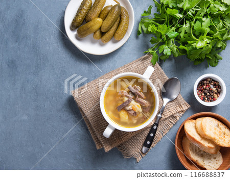 Pickle (Russian soup). Pearl soup with pickles and potatoes in a white plate on a blue background  116688837
