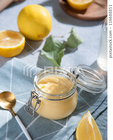 homemade lemon curd in a glass jar with lemon slices on a blue background. homemade lemon curd in a glass jar with lemon slices on a blue background. 116688851