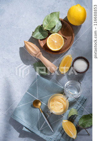 Delicious homemade lemon curd in a glass jar with lemon slices on a blue background. Delicious homemade lemon curd in a glass jar with lemon slices on a blue background. 116688853