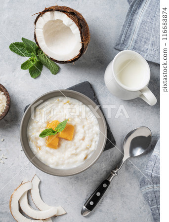 Rice porridge with coconut milk and mango slices in bowl on a blue background. Rice porridge with coconut milk and mango slices in bowl on a blue background. 116688874