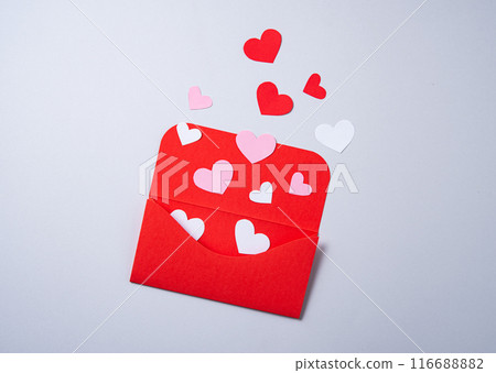 Red, pink and white paper hearts fly out of the red envelope on gray background. 116688882
