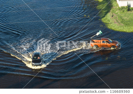 Flooded Florida road with evacuating cars and surrounded with water houses in suburban residential area. Consequences of hurricane natural disaster 116689360