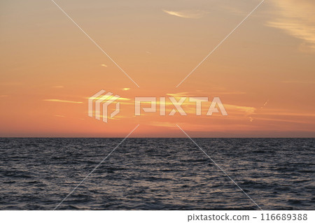 Dramatic bright red sky at ocean sunset, soft evening clouds over sea dark water 116689388