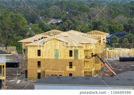 Development of residential housing in American suburbs. Unfinished frames of apartment condos with wooden roof beams under construction. Real estate market in the USA Development of residential housing in American suburbs. Unfinished frames of apartment condos with wooden roof beams under construction. Real estate market in the USA 116689399