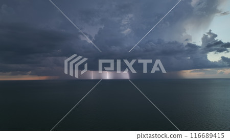 Dark ominous thunderstorm clouds forming on overcast sky during heavy rainfall season over ocean surface at sunset Dark ominous thunderstorm clouds forming on overcast sky during heavy rainfall season over ocean surface at sunset 116689415