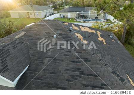 Consequences of natural disaster. Damaged house roof with missing shingles after hurricane Ian in Florida Consequences of natural disaster. Damaged house roof with missing shingles after hurricane Ian in Florida 116689438