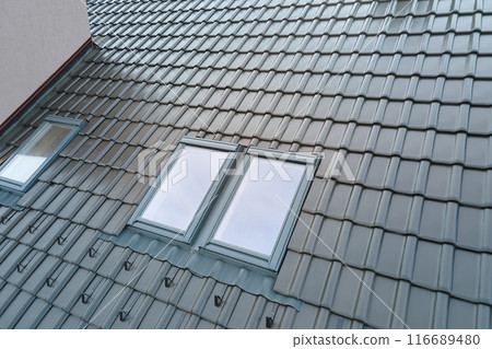 Closeup of attic window on house roof top covered with ceramic shingles. Tiled covering of building Closeup of attic window on house roof top covered with ceramic shingles. Tiled covering of building 116689480
