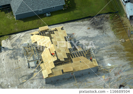 Builders working on roof construction of unfinished residential house with wooden frame structure in Florida suburban area. Housing development concept 116689504