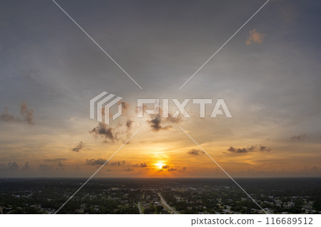 Bright sunset over dark rural land. Setting sun behind vivid orange and yellow clouds 116689512