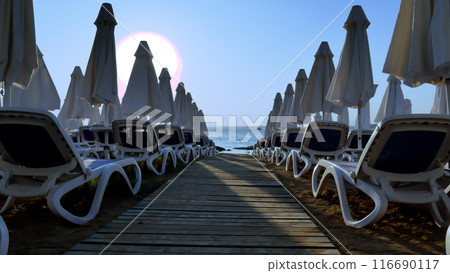 Sun loungers and folded umbrellas on the sandy beach during sunset. Evening on the beach. Sun loungers and folded umbrellas on the sandy beach during sunset. Evening on the beach. 116690117
