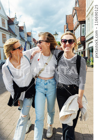 Three cheerful young adult women friend walk street old european german town city street enjoy having fun laughing sunny day together. Female persons friendship celebration party weekend Three cheerful young adult women friend walk street old european german town city street enjoy having fun laughing sunny day together. Female persons friendship celebration party weekend 116690125