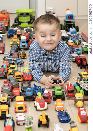 Concept of children's toys. A little boy, 4 years old, plays happily, lying on the floor, with colorful small and large cars in the children's room. 116690700