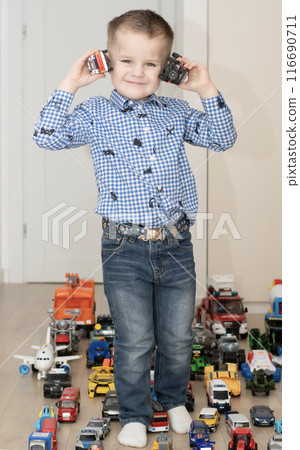 Children. Toy cars. A small cheerful and handsome boy, 4 years old, wearing a checkered shirt, plays with many colorful cars in a home interior. 116690711