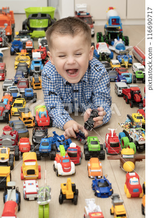 Concept of children's toys. A little boy, 4 years old, plays happily, lying on the floor, with colorful small and large cars in the children's room. Concept of children's toys. A little boy, 4 years old, plays happily, lying on the floor, with colorful small and large cars in the children's room. 116690717