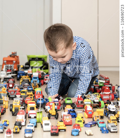 Concept of children's toys. A little boy, 4 years old, enthusiastically plays, sitting on the floor, with multi-colored small and large cars in the children's room. 116690723