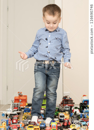 Children. Toy cars. A small cheerful and handsome boy, 4 years old, wearing a checkered shirt, plays with many colorful cars in a home interior. 116690746