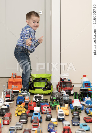 Children. Toy cars. A small cheerful and handsome boy, 4 years old, wearing a checkered shirt, plays with many colorful cars in a home interior. Children. Toy cars. A small cheerful and handsome boy, 4 years old, wearing a checkered shirt, plays with many colorful cars in a home interior. 116690756
