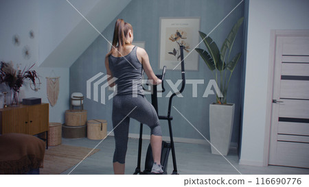 Athletic woman starts training on orbitrek. Virtual reality screen with landscape 116690776