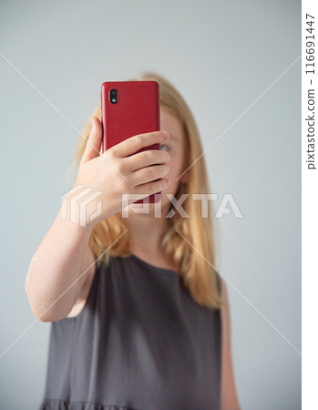 girl in a gray dress takes a video from a red mobile phone on gray background girl in a gray dress takes a video from a red mobile phone on gray background 116691447