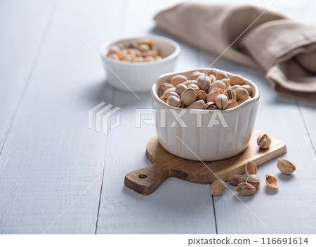 Pistachio nuts in a white bowl on a light wooden background. Front view and copy space 116691614