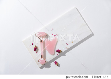flat lay with pink gua sha for face massage and dry roses on white background with hard shadows. flat lay with pink gua sha for face massage and dry roses on white background with hard shadows. 116691663