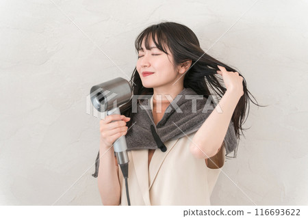 A woman blow-drying her hair with a hair dryer (hair care) 116693622