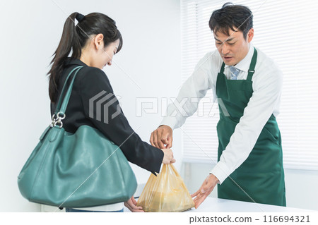 一位男性便利商店店員將便當午餐交給一位在收銀台付款的女性顧客。 一位男性便利商店店員將便當午餐交給一位在收銀台付款的女性顧客。 116694321