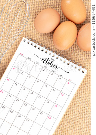 October 2024 Desk calendar and fresh eggs with egg whisk on burlap. 116694491