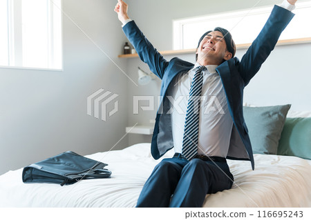A young businessman in a tired suit sitting on the bed (drinking too much, hungover, returning home in the morning, drunk) 116695243