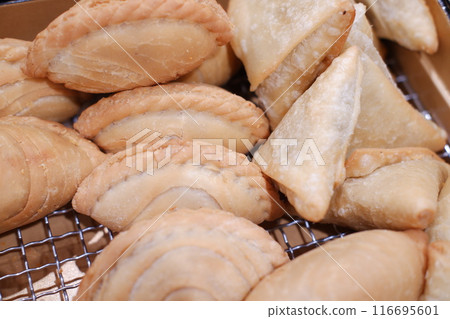 The curry puffs have a curved, layered shape, while the samosas are triangular and lightly golden brown The curry puffs have a curved, layered shape, while the samosas are triangular and lightly golden brown 116695601