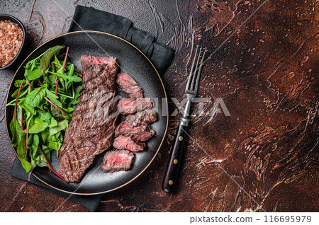Juicy Grilled Machete skirt beef meat steak on plate with salad. Dark background. Top view. Copy space 116695979