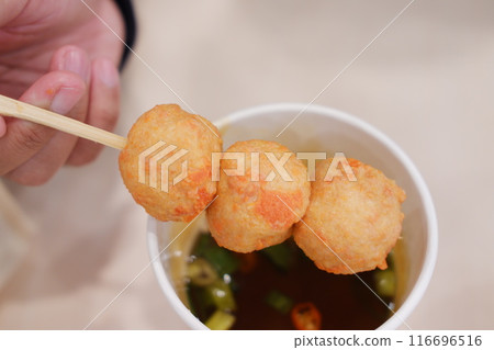 A person holds a skewer with three fried balls over a cup filled with broth and green vegetables A person holds a skewer with three fried balls over a cup filled with broth and green vegetables 116696516