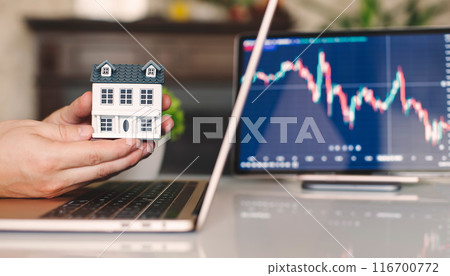Close-up of a businessman's hand holding a miniature house on a laptop screen, real estate investment, searching for a purchase Close-up of a businessman's hand holding a miniature house on a laptop screen, real estate investment, searching for a purchase 116700772