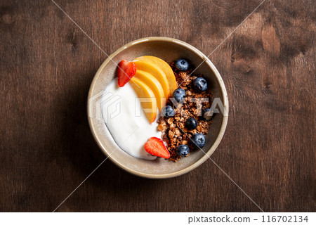 Fresh natural yogurt with homemade granola, peach, strawberry and blueberry in a bowl  116702134