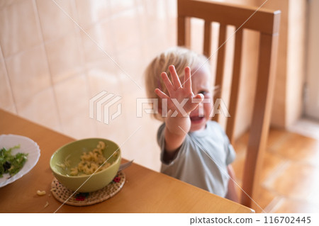 Beautiful blond child eating and crying with tantrum at home. 116702445