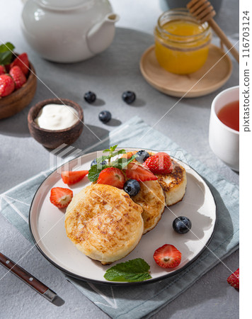 Pancakes with cottage cheese or syrniki with fresh blueberries, strawberries, honey and sour cream Pancakes with cottage cheese or syrniki with fresh blueberries, strawberries, honey and sour cream 116703124