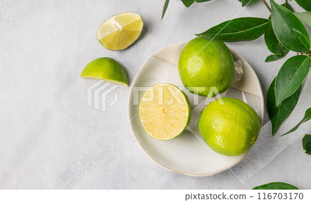 Fresh juicy limes in a plate on a light background with leaves and citrus pieces. 116703170