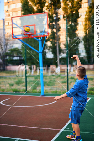 caucasian little basketball player jumps to throw the ball into the basket hoop 116703568