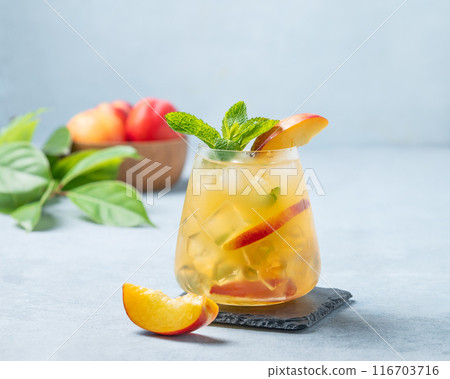 Refreshing peach cocktail, lemonade or iced tea in a glass on a light background. Refreshing peach cocktail, lemonade or iced tea in a glass on a light background. 116703716