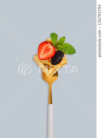 Wafer pieces with fresh strawberries, blackberries, mint leaves  on a fork on a blue background 116703793