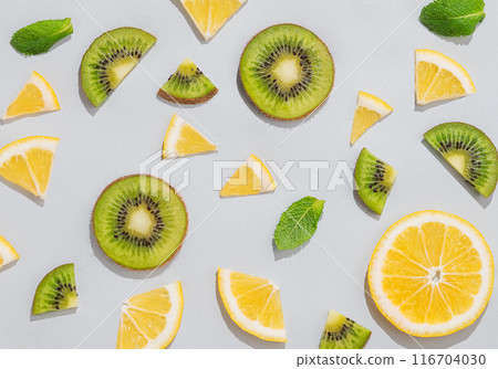 Pattern of juicy slices of lemons, kiwi fruits and mint leaves on a light background with shadow. Pattern of juicy slices of lemons, kiwi fruits and mint leaves on a light background with shadow. 116704030