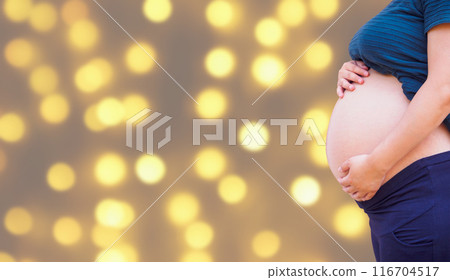 pregnant woman holding her pregnant belly over holiday bokeh lights background 116704517