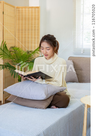 Young woman sitting and reading a book from the couch. Young woman sitting and reading a book from the couch. 116705020