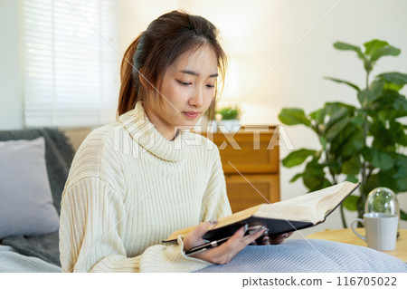 Young woman sitting and reading a book from the couch. 116705022
