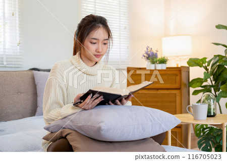 Young woman sitting and reading a book from the couch. Young woman sitting and reading a book from the couch. 116705023