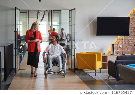 A group of young business people in a modern glass-walled office captures the essence of diversity and collaboration, while two colleagues, including an African American businessman in a wheelchair 116705437