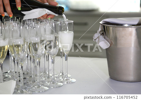 The waiter pours champagne into glasses. Champagne on the table at the restaurant. The waiter pours champagne into glasses. Champagne on the table at the restaurant. 116705452