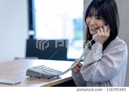 Middle-aged woman talking on a landline phone in the office 116705485