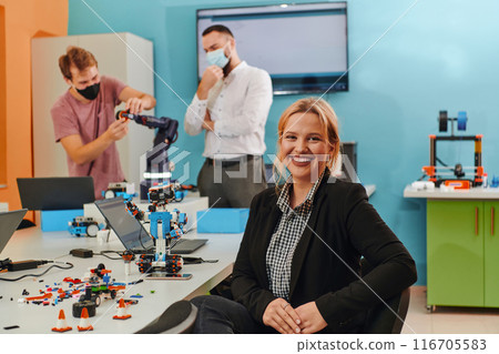 A woman sitting in a laboratory while her colleagues test a new robotic invention in the background 116705583