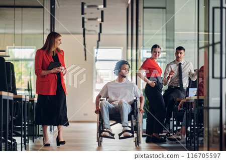 A group of young business people in a modern glass-walled office captures the essence of diversity and collaboration, while two colleagues, including an African American businessman in a wheelchair A group of young business people in a modern glass-walled office captures the essence of diversity and collaboration, while two colleagues, including an African American businessman in a wheelchair 116705597